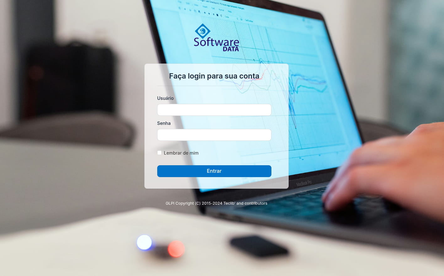 Preview da tela de login do sistema utilizado pela empresa SoftwareDATA. A imagem possui ao fundo aparece as mãos de uma pessoa utilizando o notebook e um formulário de login para acesso ao sistema.